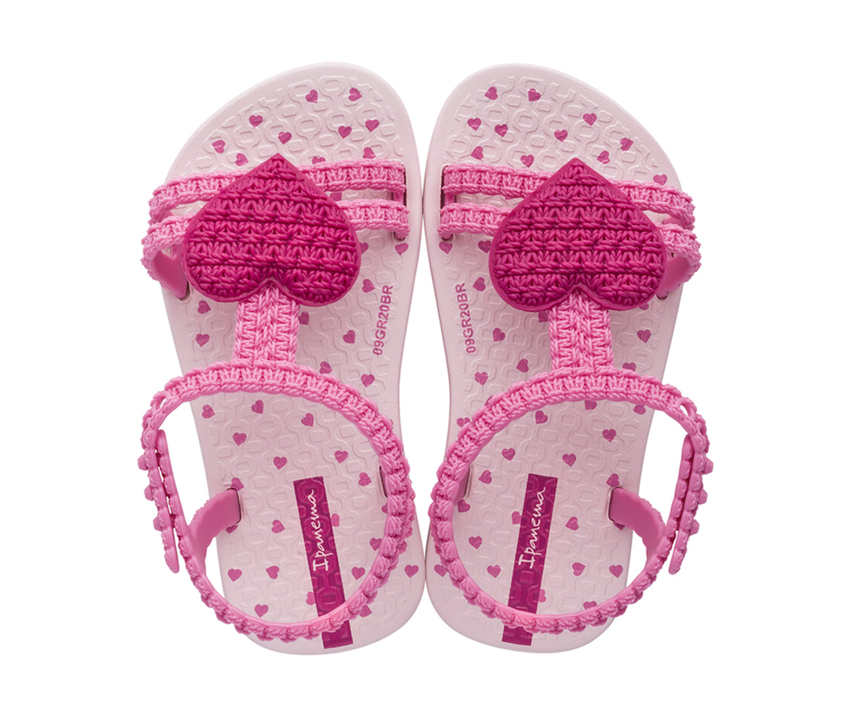 Top view of a pari of pink My First Ipanema Sandals with straps and a crochet heart on top.